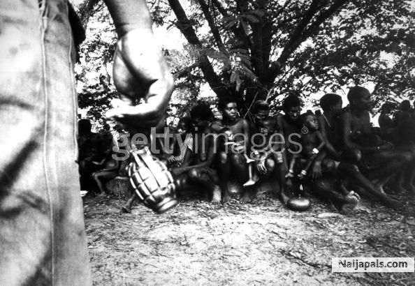 A federal soldier swings a hand grenade by its release pin while guarding Igbo women prisoners and their children in Nigeria, during the Biafran War - click for next photo
